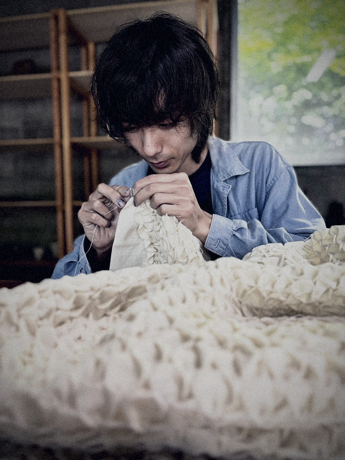 Artisan stitching shibori by the workshop shelves