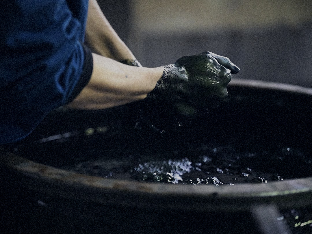 Wringing cloth over the vat, hands stained deep indigo