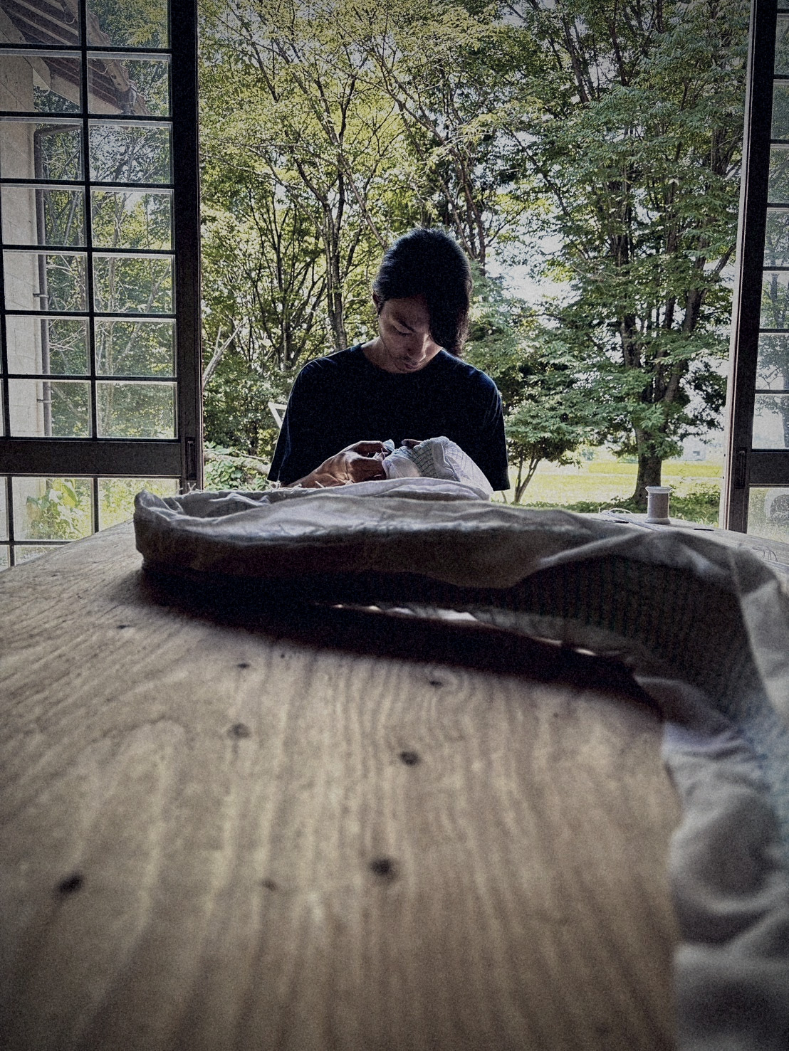 Artisan stitching cloth by open shoji doors, summer fields beyond